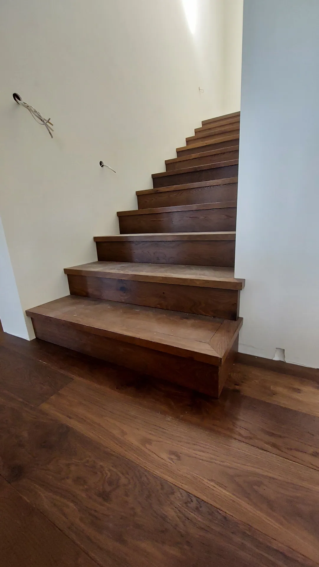 The bottom of a closed staircase clad in dark oak treads and risers, rising from a matching oak floor.