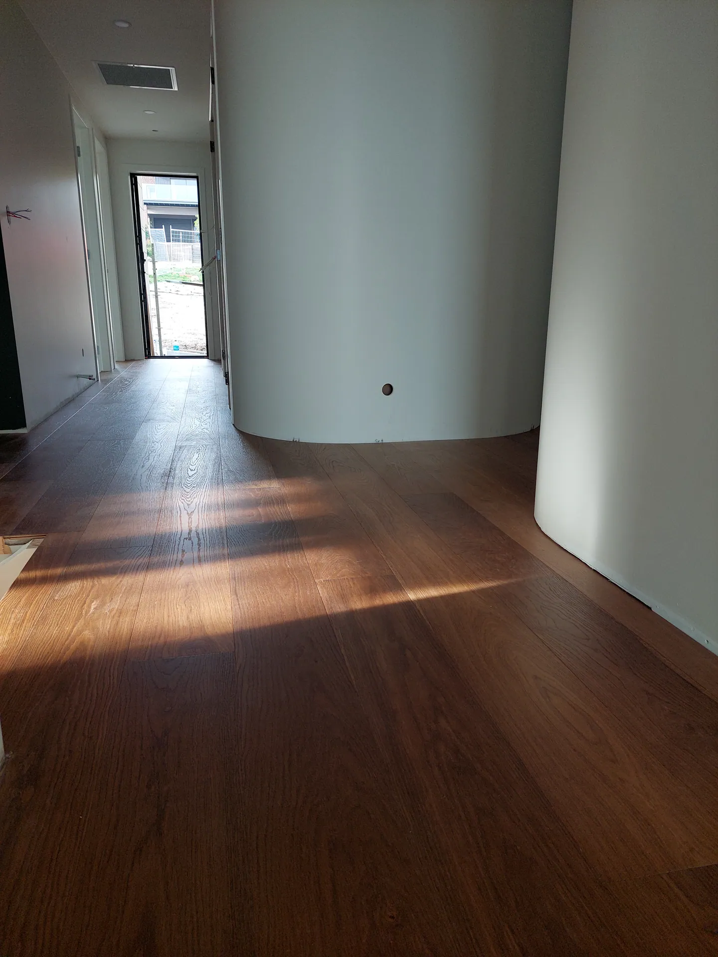 Hallway with dark timber floorboards in afternoon sun beside a curved white wall.