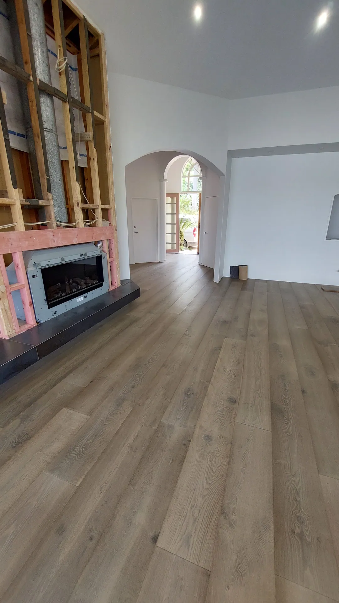 Wide grey-brown oak boards in a living room beside a framed-up fireplace still awaiting cladding.