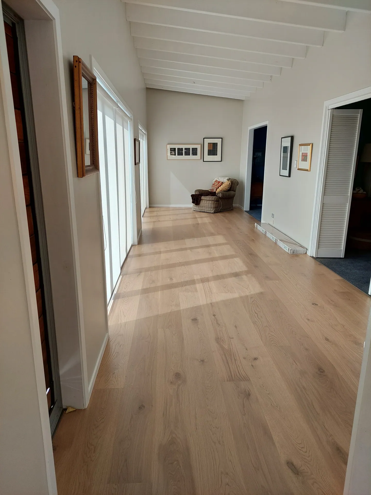 Furnished hallway with light oak floorboards and sunlight coming through glass doors.
