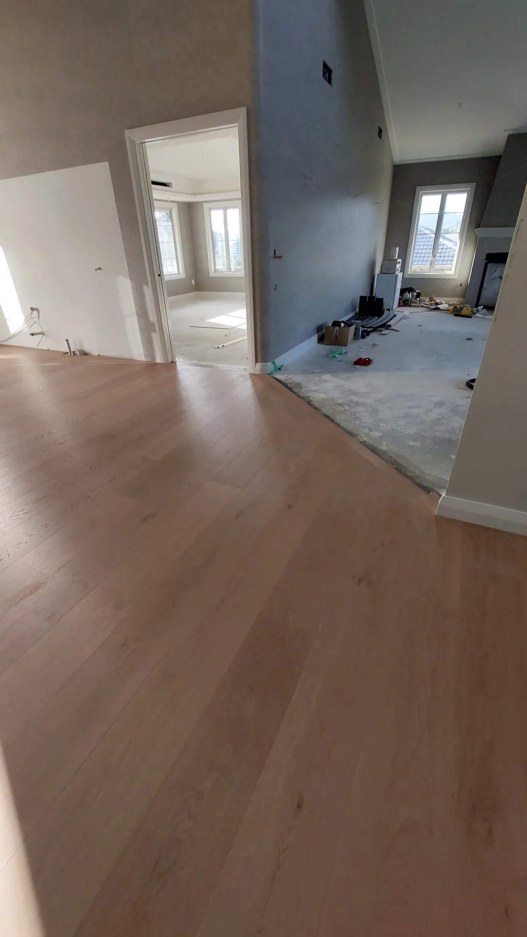 A newly laid light oak floor beside a doorway into a room with bare concrete and building materials.