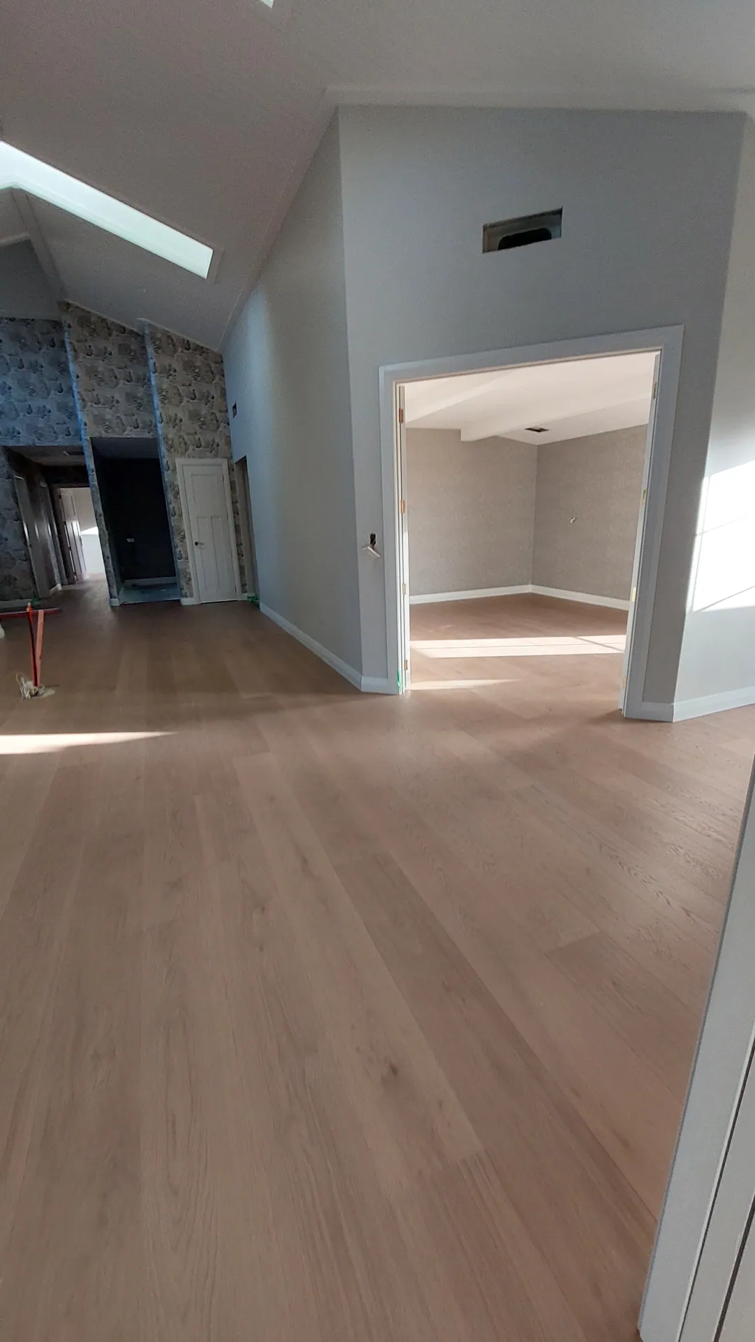 A light oak floor running through a hallway with a skylight and into a carpeted bedroom.