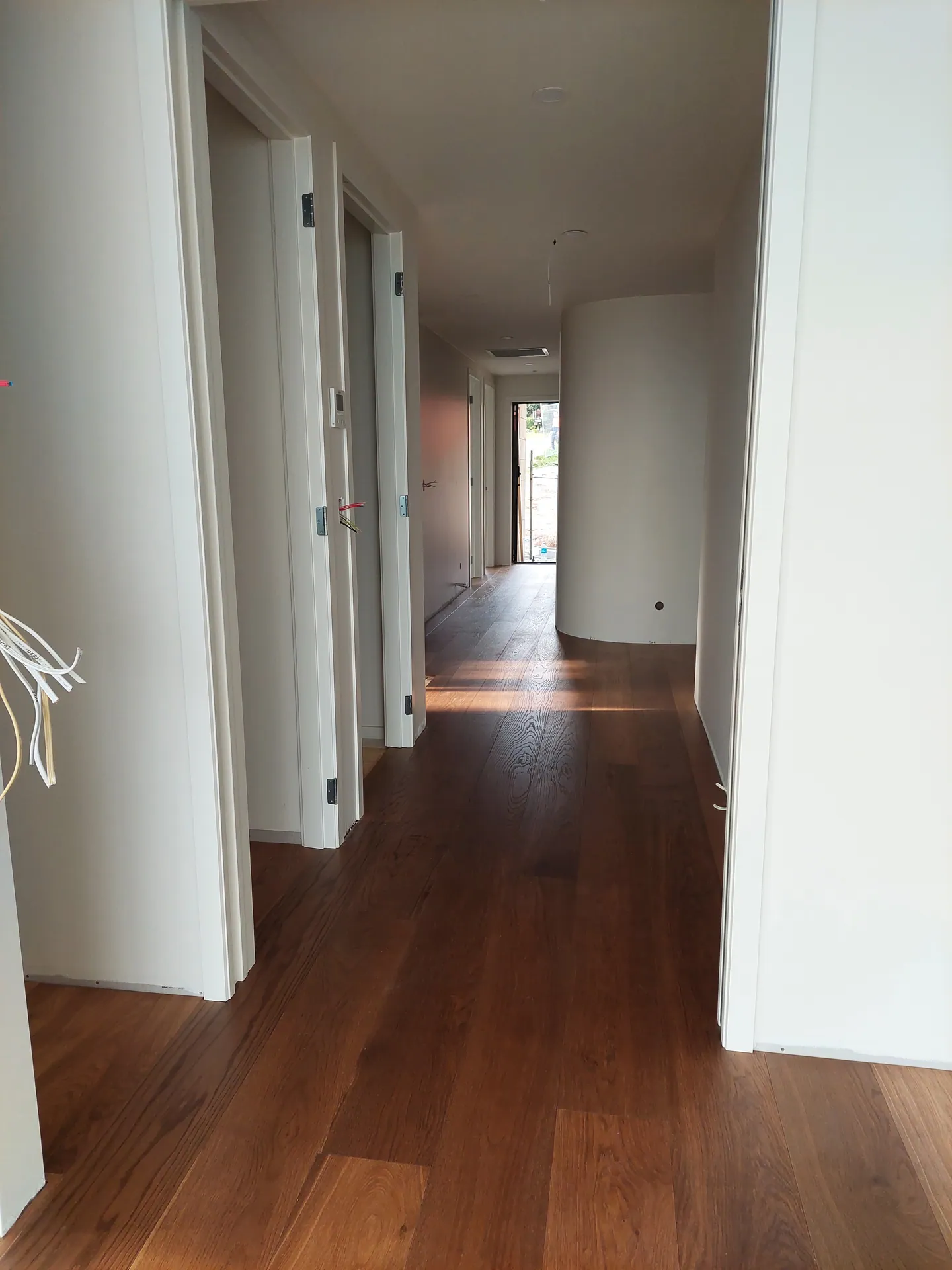 Long hallway with dark timber floorboards and white doors leading to a curved wall.
