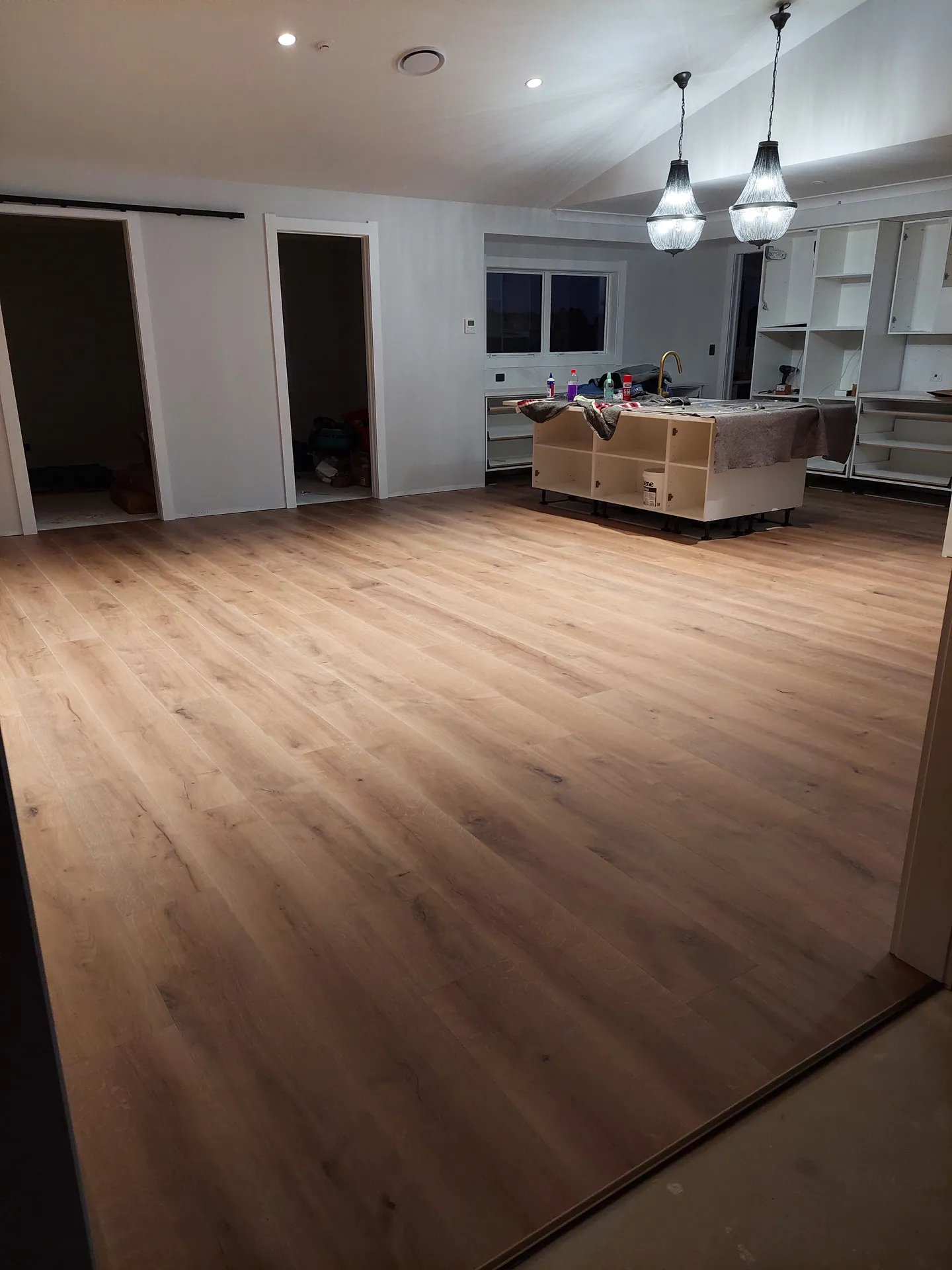 Evening view of a new timber-look floor across a large living area with a kitchen being fitted.