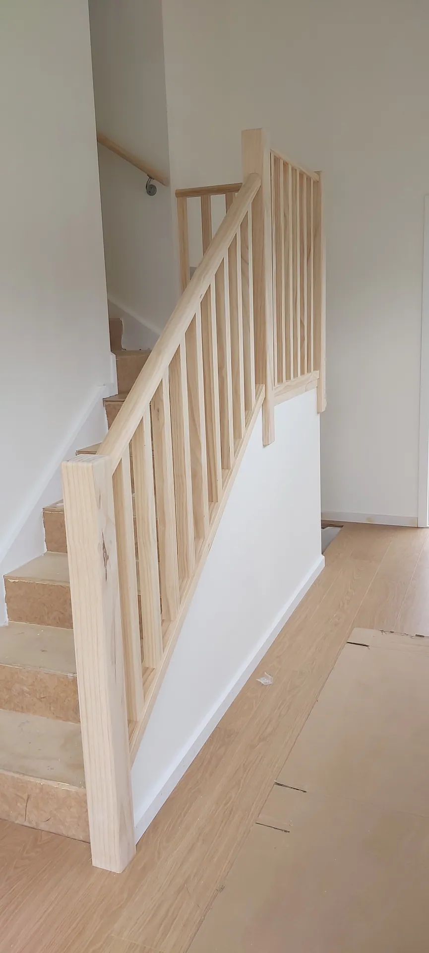 Staircase with a new pine balustrade and plywood treads, with the floor below protected by cardboard.