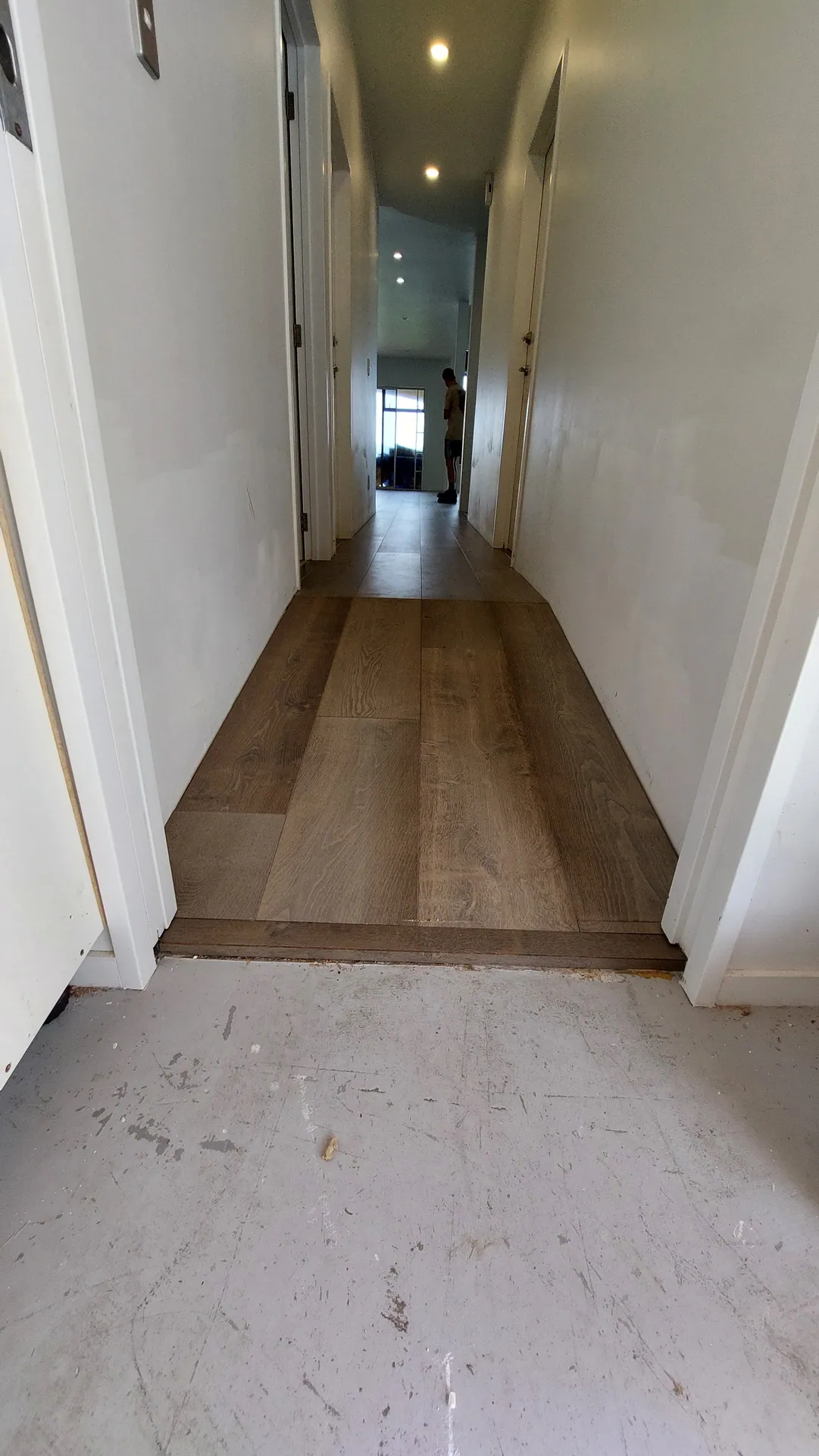 A hallway with grey-brown oak boards laid up to an unfinished section of bare subfloor in the foreground.