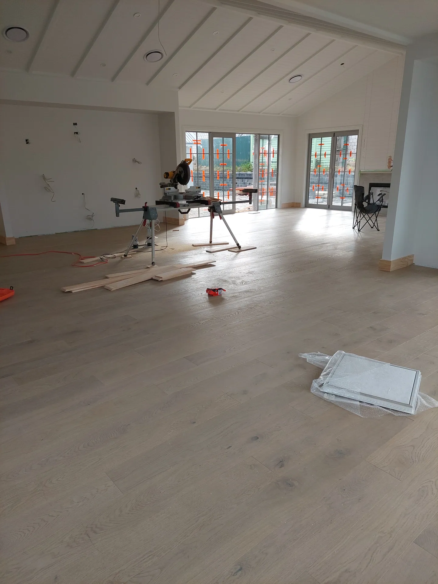 Open-plan room with a light oak floor being laid, a mitre saw and offcuts on the floor.