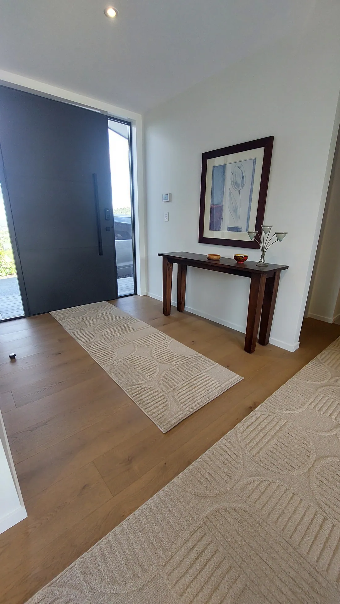 An entry with an oak floor, a tall dark pivot door, a console table and patterned runner rugs.