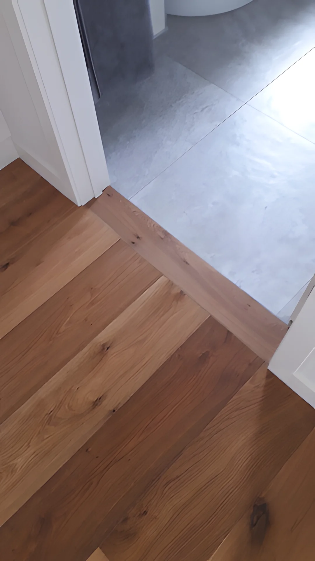 Oak floor meeting grey tiles at a doorway.