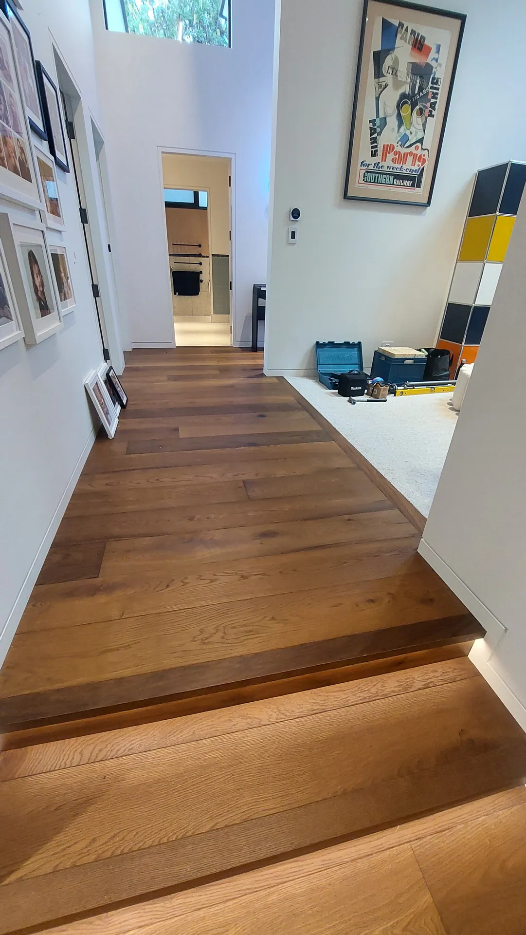 An oak-floored hallway with a single step lit by a strip light, and framed pictures along the wall.