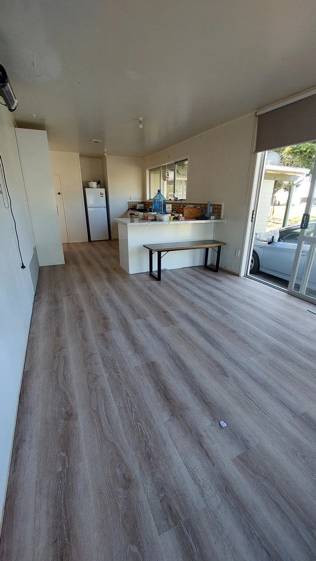 An oak-look plank floor in a living area running to a kitchen bench, with a sliding door to a carport.