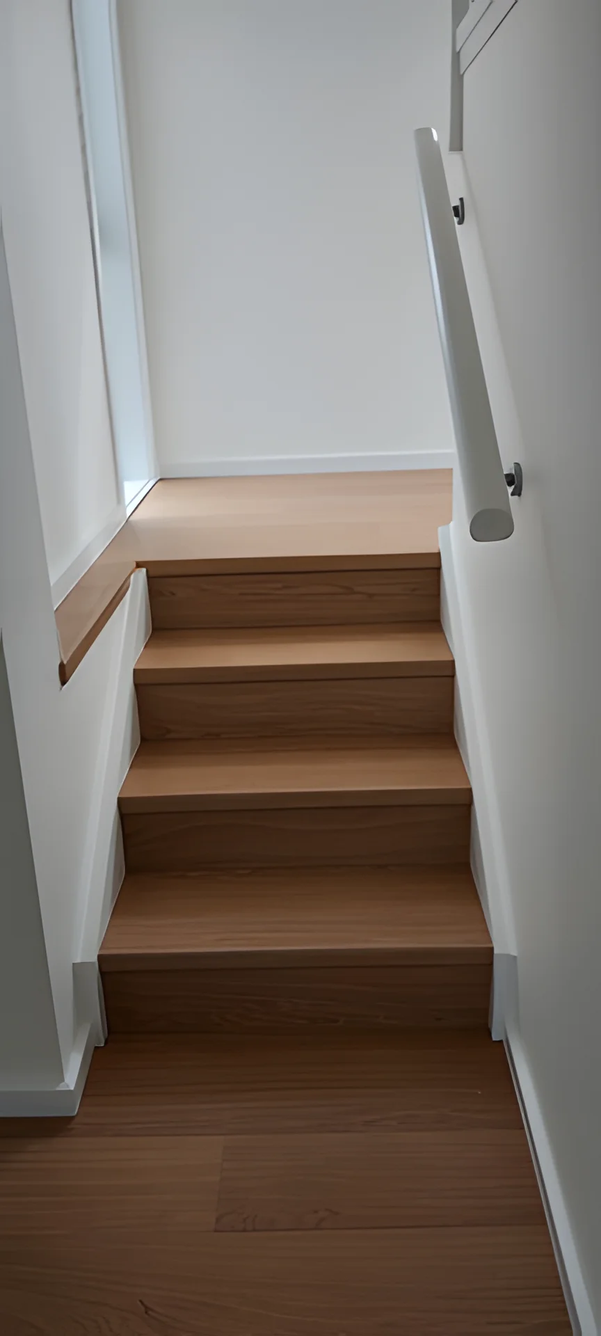 Short flight of timber stair treads and risers between white walls with a white wall-mounted handrail.