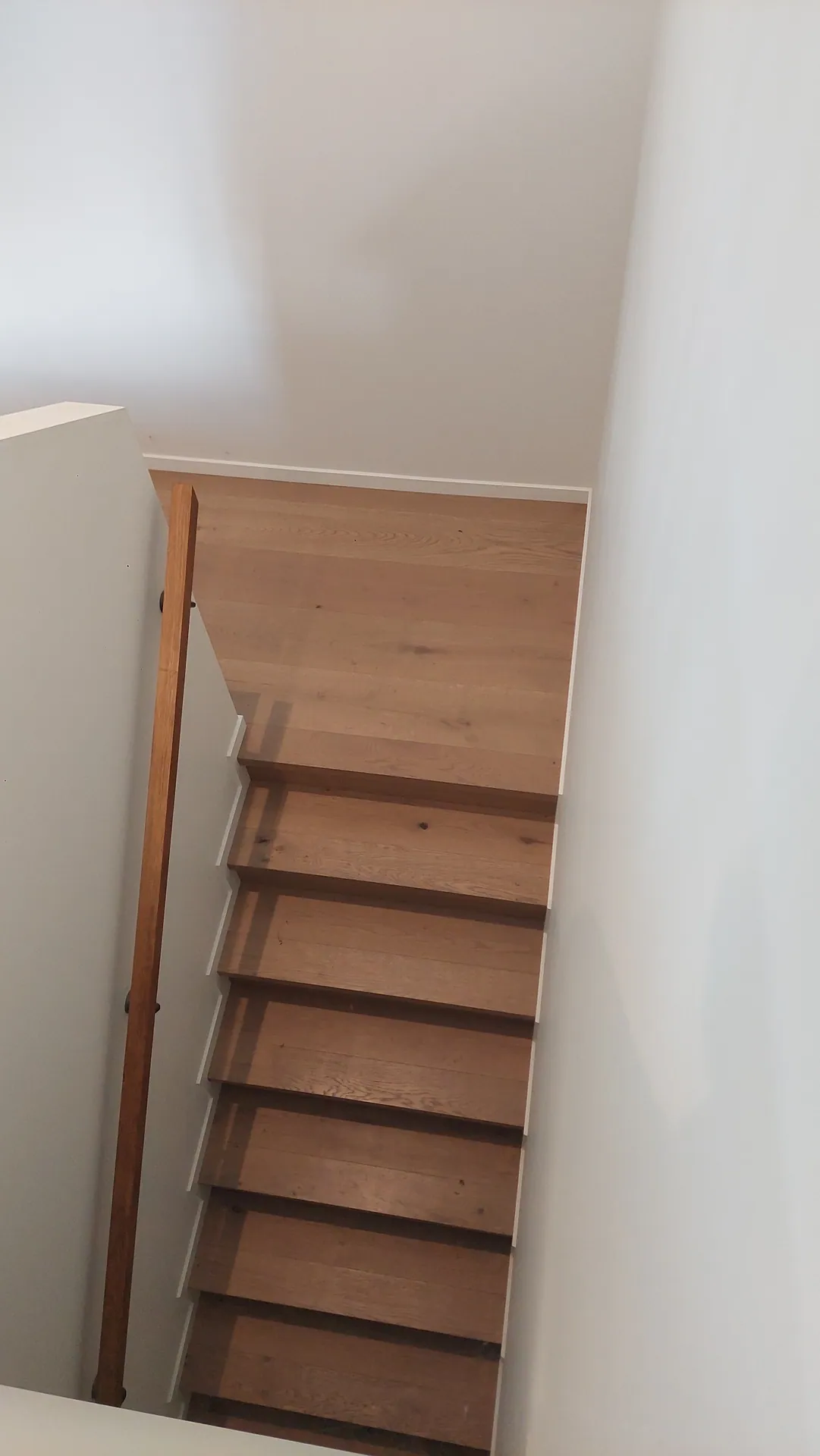 A straight run of oak stair treads and risers seen from above, with a timber handrail on one side.