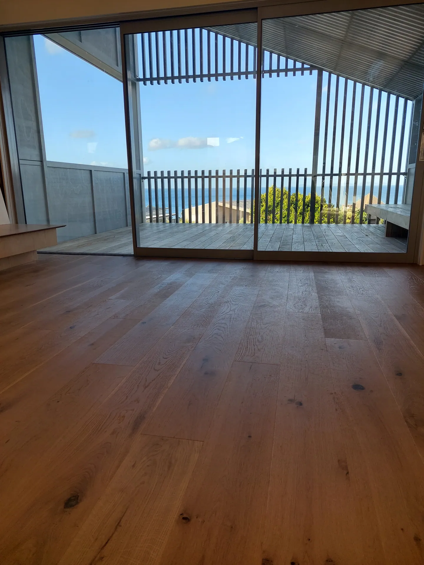 Wide knotty oak floorboards leading to sliding doors, a deck with timber slats and the sea beyond.