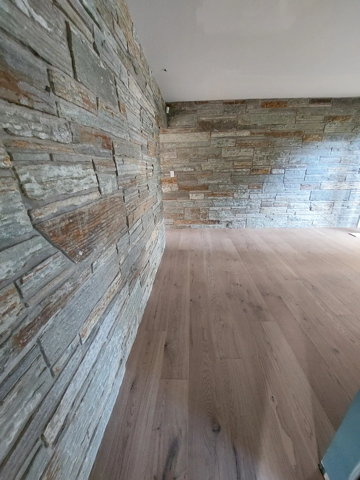 Grey-toned wide plank timber floor in a room with stacked stone walls on two sides.